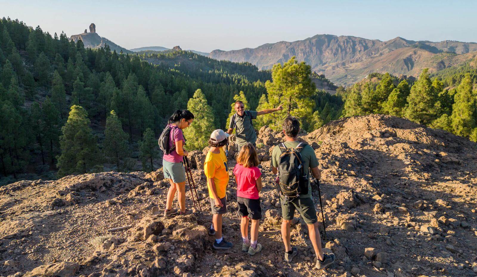 Turgruppe i Landsbygdparken ved Roque Nublo, med steingrunn, kanarifurulund og fjelltoppen i bakgrunnen.