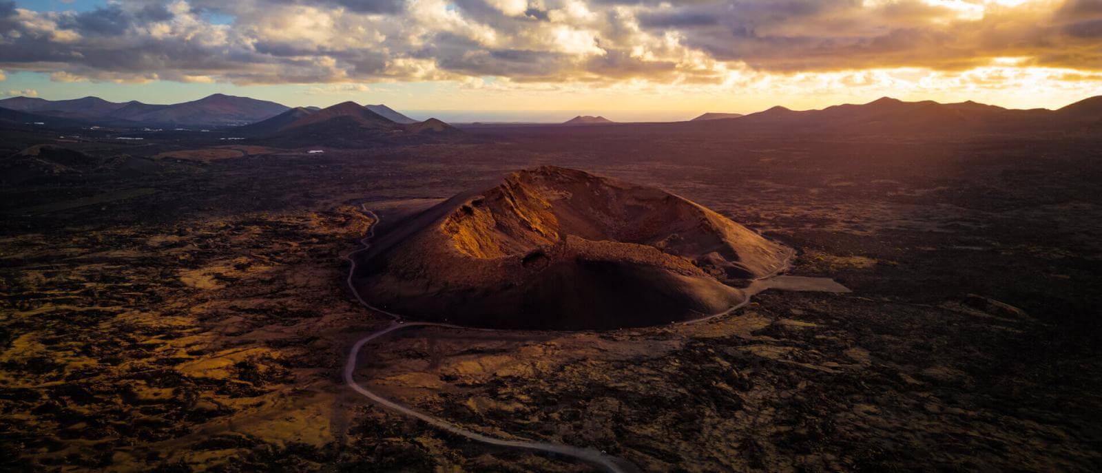 Fugleperspektiv over Cuervo-Vulkanen på Lanzarote, med opplyst krater i solnedgangen.