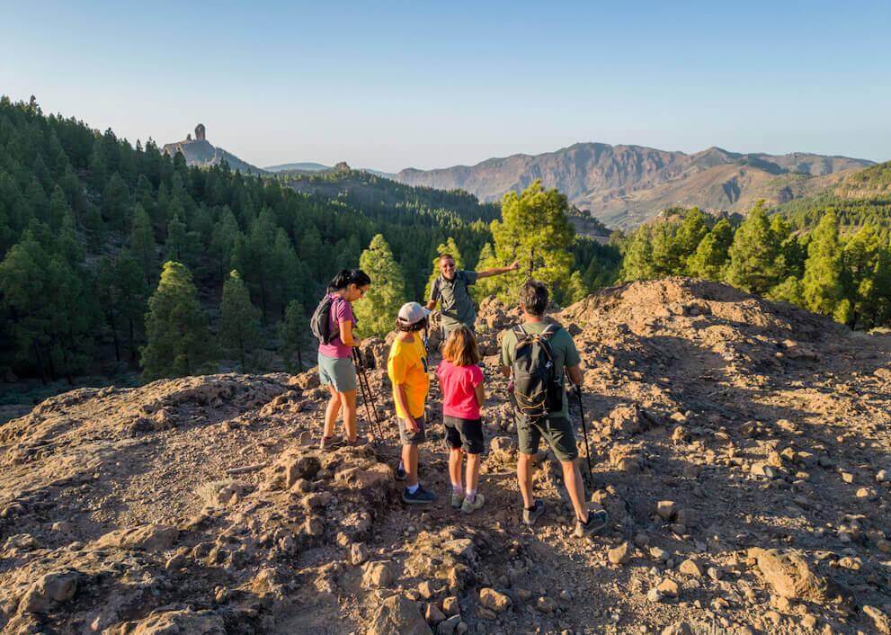 Turgruppe i Landsbygdparken ved Roque Nublo, med steingrunn, kanarifurulund og fjelltoppen i bakgrunnen.