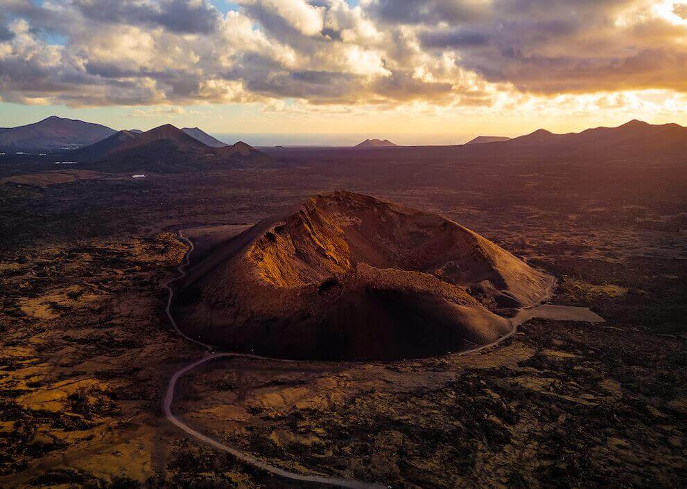 Fugleperspektiv over Cuervo-Vulkanen på Lanzarote, med opplyst krater i solnedgangen.