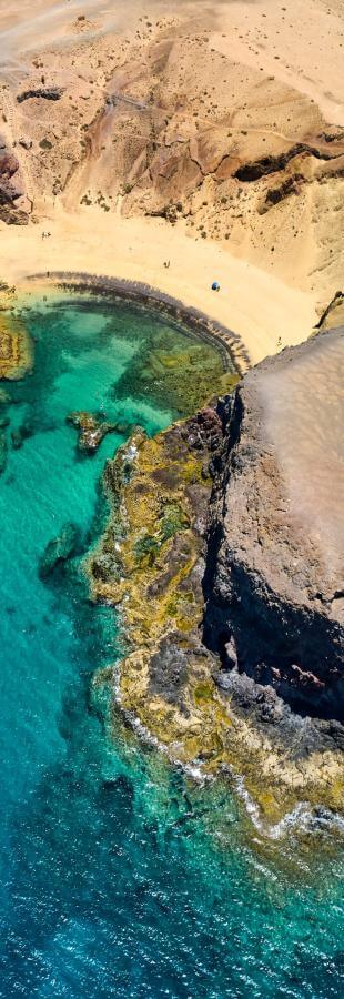 Fugleperspektiv over Papagayo-stranden på Lanzarote, med gyllen sand, vulkanske klipper og turkist sjøvann.