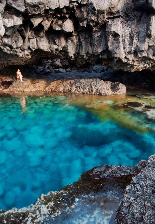 Charco Azul på El Hierro, en naturlig kulp med turkist vann omgitt av mørk vulkanstein under en klippevegg.