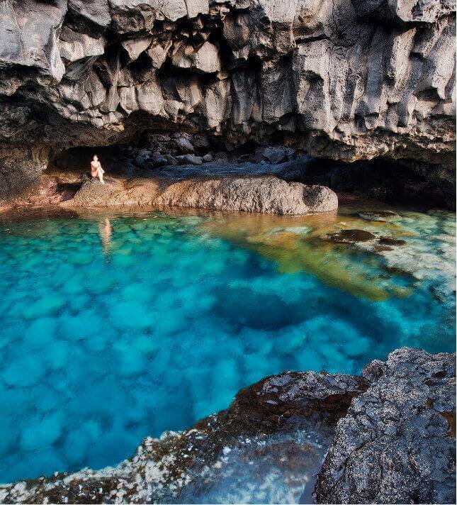 Charco Azul på El Hierro, en naturlig kulp med turkist vann omgitt av mørk vulkanstein under en klippevegg.